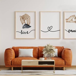 Può includere: Tre stampe artistiche incorniciate con le parole "amore" e "famiglia" in corsivo. Le stampe presentano illustrazioni di mani e un cuore. Le stampe sono esposte sopra un divano arancione con un cuscino bianco.