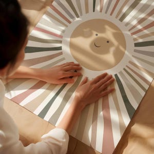 Pode incluir: Um fundo branco com um grande sol marrom com um rosto sorridente no centro. O sol é cercado por listras coloridas em tons de marrom, rosa e verde.