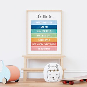 Op de afbeelding: Een ingelijst print met een regenboogachtergrond en de tekst "It's Ok to..." gevolgd door een lijst met zinnen, waaronder "Make Mistakes", "Say No", "Ask for Help", "Have Bad Days", "Start Over", "Not Know Everything" en "Be Yourself".