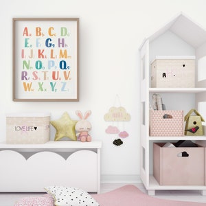 May include: A white bookshelf shaped like a house with three shelves. The top shelf has a beige box with a pink heart and the text "LOVE" on it. The middle shelf has a stack of books. The bottom shelf has a pink box with a geometric pattern and a birdhouse with a red bird on it. There is a white storage bench with a scalloped edge and a beige box with the text "LOVE LIFE" on it. There is a gold star, a white bunny, and a cloud with the text "DREAM" on it.