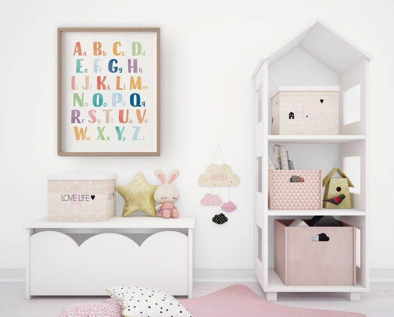 May include: A white bookshelf shaped like a house with three shelves. The top shelf has a beige box with a pink heart and the text "LOVE" on it. The middle shelf has a stack of books. The bottom shelf has a pink box with a geometric pattern and a birdhouse with a red bird on it. There is a white storage bench with a scalloped edge and a beige box with the text "LOVE LIFE" on it. There is a gold star, a white bunny, and a cloud with the text "DREAM" on it.
