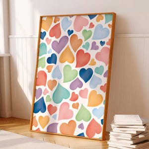 Könnte beinhalten: Ein gerahmter Kunstdruck mit einem Muster aus bunten Aquarellherzen in Rot-, Orange-, Gelb-, Grün-, Blau- und Lilatönen. Die Herzen sind auf weißem Hintergrund angeordnet, und der Rahmen ist aus Holz.