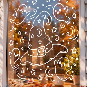 May include: A white window decal featuring a central witch hat with a buckle, surrounded by four small ghosts, various stars, and swirling patterns. The design is rendered in a simple line art style, creating a festive Halloween decoration.