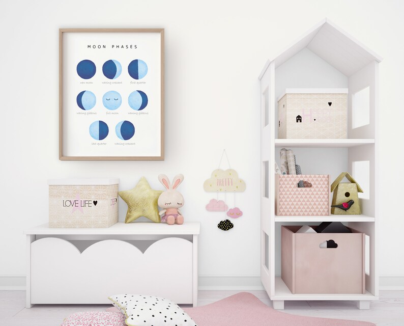 May include: A white bookshelf shaped like a house with three shelves. The top shelf has a pink and white storage box with a house design and the text "Home". The middle shelf has a stack of books. The bottom shelf has a pink and white storage box with a geometric pattern and a small birdhouse with a red bird.