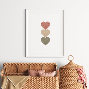 May include: A framed print with three watercolor hearts in shades of pink, beige, and green. The hearts are arranged vertically in a row.