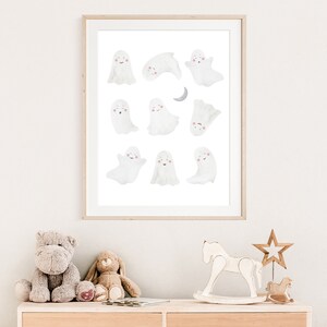 Puede incluir: Una impresi&oacute;n enmarcada de una ilustraci&oacute;n de acuarela con 10 fantasmas blancos con mejillas rosadas. Los fantasmas est&aacute;n en varias poses, incluyendo volar, dormir y sonre&iacute;r. Una luna creciente est&aacute; en la esquina superior derecha de la impresi&oacute;n.