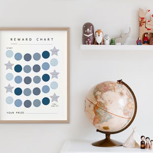 May include: A blue and white reward chart with a grid of circles and stars. The chart has the text "REWARD CHART" at the top and "YOU DID IT!" at the bottom. The chart is framed in wood and is hanging on a white wall.