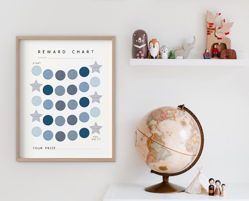May include: A blue and white reward chart with a grid of circles and stars. The chart has the text "REWARD CHART" at the top and "YOU DID IT!" at the bottom. The chart is framed in wood and is hanging on a white wall.