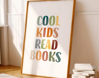 Pode incluir: Uma impressão artística emoldurada com as palavras "COOL KIDS READ BOOKS" em letras coloridas e lúdicas. A moldura de madeira envolve um fundo branco. Uma pilha de livros repousa no chão perto da obra de arte, sugerindo um quarto infantil ou um canto de leitura.