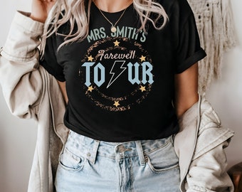 May include: Black t-shirt with a distressed circle graphic featuring the text "Mrs. Smith's Farewell Tour" in a blue and white font with a lightning bolt and yellow stars.