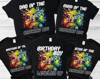 Könnte beinhalten: Satz von fünf schwarzen T-Shirts mit einer bunten Grafik einer Videospielkonsole und Text, der "Papa des Geburtstagskindes", "Mama des Geburtstagskindes", "Bruder des Geburtstagskindes", "Geburtstagskind Level Up" und "Schwester des Geburtstagskindes" lautet.