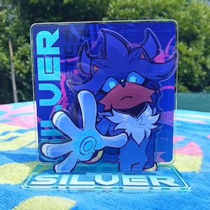 May include: A clear acrylic standee featuring a stylized blue character with spiky hair and glowing eyes, reaching forward with an open hand. The background panel displays a blue circuit board pattern and the vertical text SILVER. The base reads SILVER.