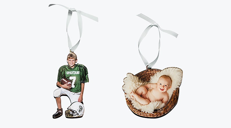 May include: Two custom photo ornaments with white ribbon hangers. One ornament features a child in a green Spartans football jersey holding a football with a helmet nearby. The other ornament shows a baby lying in a brown woven basket with fur.