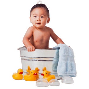 May include: A young child sits inside a round, silver-colored metal wash tub. Three yellow rubber ducks with orange beaks are positioned in front of the tub, and a light blue towel is draped over the side of the metal container.