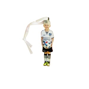 May include: A flat, die-cut ornament featuring a child in a white and black soccer uniform with the text "TOTTENHAM" on the shirt, holding a soccer ball with a blue and red star pattern. A white ribbon is attached to the top for hanging purposes.