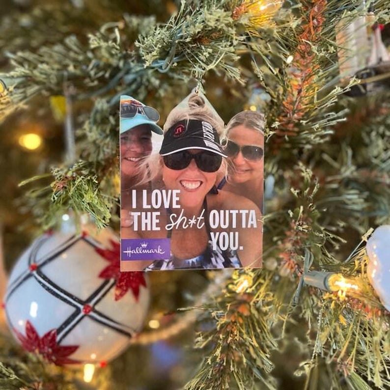 May include: A rectangular Christmas tree ornament featuring a photograph of three people wearing sunglasses and hats. The text "I LOVE THE SH*T OUTTA YOU." is printed in white over the image, with the Hallmark logo in the bottom left corner.