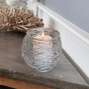 May include: A silver wire candle holder with a white candle inside. The candle holder is on a grey countertop.