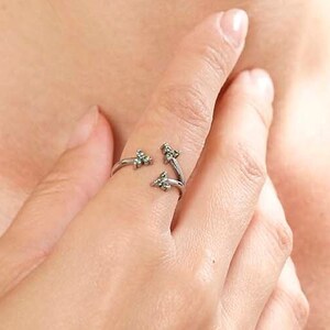 May include: A silver ring with three small green gemstones. The ring is worn on the index finger of a person's hand.