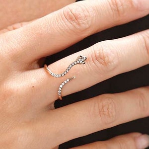 Op de afbeelding: Een gouden slangenring met een met diamanten bezet lichaam. De ring is open en wikkelt zich om de vinger.