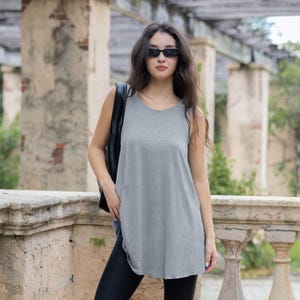 May include: A woman wearing a gray sleeveless top with a black bag slung over her shoulder. She is wearing black leggings and sunglasses.