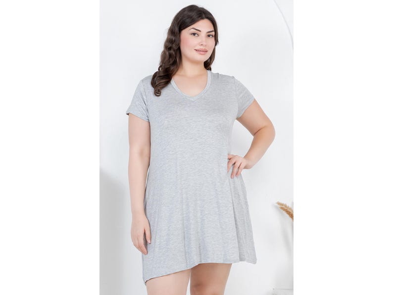 Puede incluir: Un vestido gris claro de manga corta con cuello en V. El vestido tiene una falda acampanada y est&aacute; hecho de un material suave y c&oacute;modo. La modelo lleva el vestido y tiene la mano en la cadera.