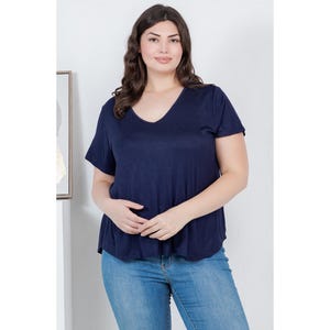 Op de afbeelding: Een marineblauw V-hals T-shirt met korte mouwen. Het shirt wordt gecombineerd met lichtblauwe jeans. Het model staat voor een witte muur met een ingelijste foto.
