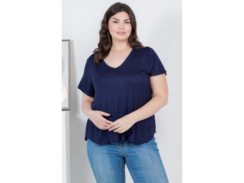 Op de afbeelding: Een marineblauw V-hals T-shirt met korte mouwen. Het shirt wordt gecombineerd met lichtblauwe jeans. Het model staat voor een witte muur met een ingelijste foto.