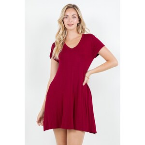 Puede incluir: Un vestido corto burdeos con cuello en V y mangas cortas. El vestido tiene una falda acampanada y est&aacute; hecho de una tela suave y fluida. La modelo lleva una pulsera en la mu&ntilde;eca.