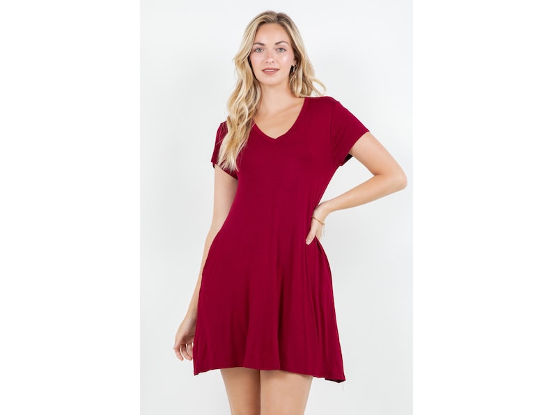 Puede incluir: Un vestido corto burdeos con cuello en V y mangas cortas. El vestido tiene una falda acampanada y est&aacute; hecho de una tela suave y fluida. La modelo lleva una pulsera en la mu&ntilde;eca.