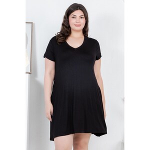 Puede incluir: Un vestido negro con cuello en V y mangas cortas. El vestido tiene un dise&ntilde;o sencillo y fluido y llega hasta la rodilla. La modelo lleva el vestido en un estudio con un fondo neutro.