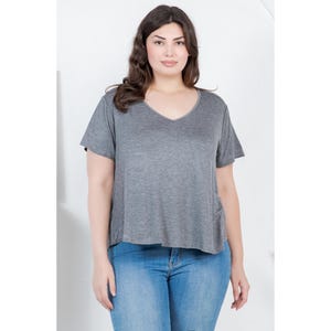 Op de afbeelding: Een grijs V-hals T-shirt met korte mouwen. Het shirt wordt gecombineerd met lichtblauwe jeans. Het model staat voor een witte achtergrond. Het shirt heeft een relaxte pasvorm.