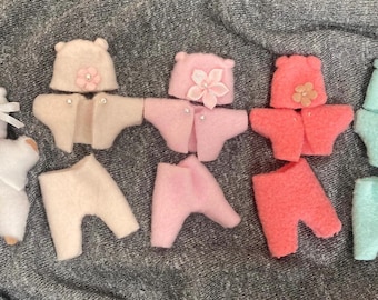 May include: A collection of five miniature doll outfits made of felt, each including a hat, a jacket, and pants. The sets come in white, beige, light pink, coral, and mint green, with decorative fabric flowers and small white beads.