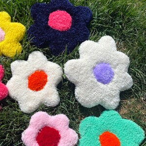 May include: A collection of colorful, fluffy, flower-shaped cushions with different colored centers. The cushions are arranged on a bed of green grass.