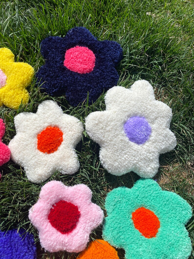 May include: A collection of colorful, fluffy, flower-shaped cushions with different colored centers. The cushions are arranged on a bed of green grass.