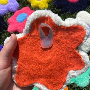 May include: A bright orange felt flower with a white fuzzy border. The back of the flower has a white loop for hanging.