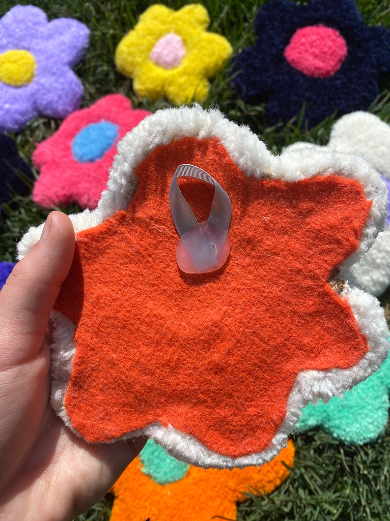 May include: A bright orange felt flower with a white fuzzy border. The back of the flower has a white loop for hanging.