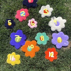 May include: Twelve colorful flower-shaped rugs with numbers 1 through 12 on a green grassy lawn.