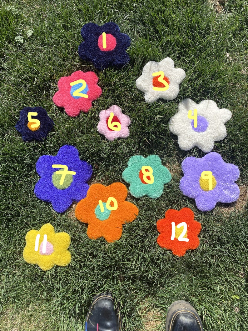 May include: Twelve colorful flower-shaped rugs with numbers 1 through 12 on a green grassy lawn.