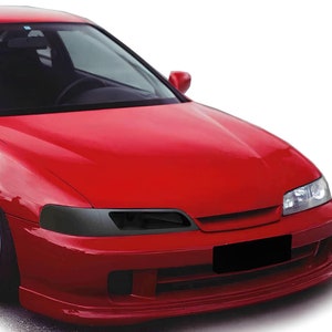 Pode incluir: Um Honda Integra vermelho com faróis escurecidos e rodas brancas. O carro tem um pára-choques dianteiro preto e uma grelha preta.