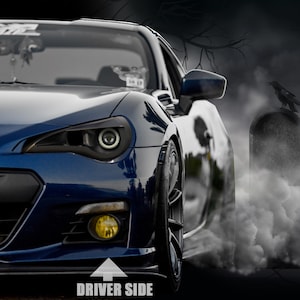 Puede incluir: Un coche deportivo azul con faros negros y luces antiniebla amarillas. La parte delantera del coche es visible, con las palabras "DRIVER SIDE" y una flecha que apunta hacia el lado del conductor. Una lápida y un cuervo están en el fondo.