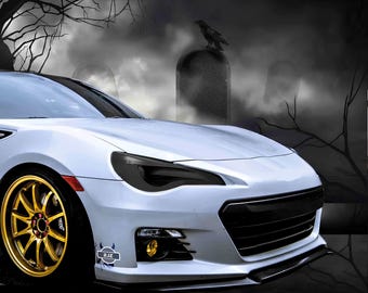May include: A white sports car with black headlights and a black grille. The car is parked in front of a spooky background with trees and fog.