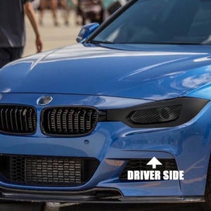 Puede incluir: Parte frontal de un coche azul, con una parrilla, faros y parachoques negros. La imagen muestra el lado del conductor con el texto "DRIVER SIDE" en blanco. El coche tiene un diseño moderno, centrado en el rendimiento.
