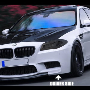 Może przedstawiać: Biało-czarny luksusowy sedan z czarnymi felgami i czarną maską. Samochód ma niski profil i jest w ruchu. Tekst "DRIVER SIDE" jest widoczny na dole obrazu.