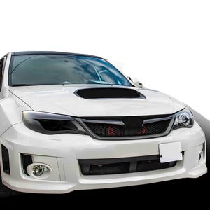 Könnte beinhalten: Weißer Subaru Impreza mit geschwärzten Scheinwerfern, einem schwarzen Gittergrill und einer schwarzen Motorhaubenabdeckung.