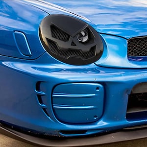 Pode incluir: Um Subaru Impreza WRX azul com uma grade e faróis pretos de reposição. O carro tem um spoiler dianteiro e um difusor traseiro pretos.