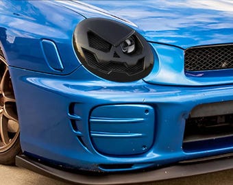 May include: A blue Subaru Impreza WRX with a black aftermarket grille and headlights. The car has a black front lip spoiler and a black rear diffuser.