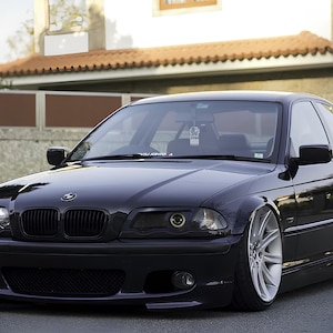 May include: A black BMW 3 Series saloon with aftermarket wheels and a lowered suspension. The car has a black grille and headlights, and the front bumper has a lip spoiler.