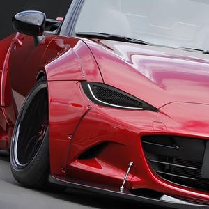 Może przedstawiać: Czerwony samochód sportowy z czarnymi reflektorami i czarną kratką. Samochód ma szeroki pakiet nadwozia i duże koła.