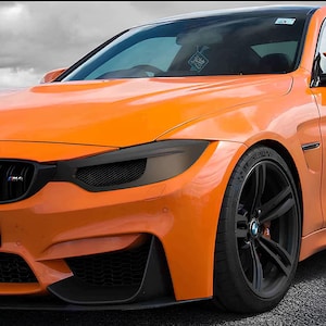 Könnte beinhalten: Ein leuchtend orangefarbener Sportwagen mit schwarzen Felgen und einem schwarzen Kühlergrill. Das Auto hat getönte Scheiben und ein elegantes, modernes Design.