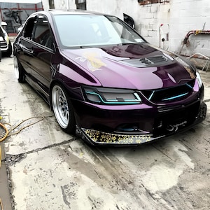 Puede incluir: Un coche morado con detalles dorados y un alerón delantero negro. El coche tiene una parrilla negra y faros negros. El coche está aparcado en una superficie de hormigón.